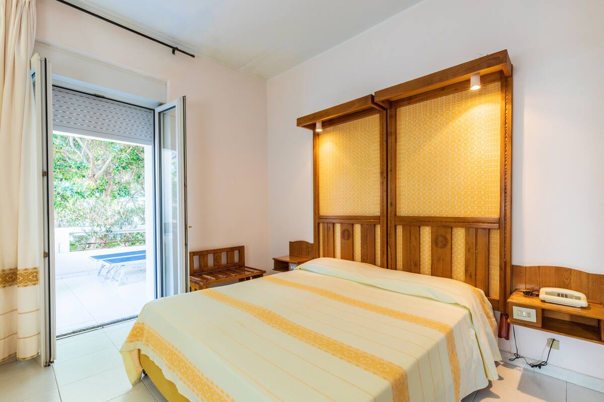 A bedroom with a bed, a bedside table, a nightstand, and a window with curtains.
