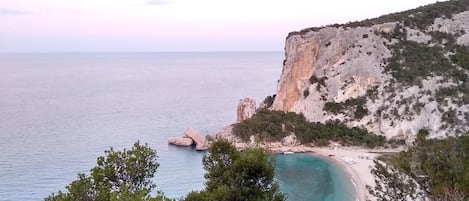 A coastal landscape with a cliff, beach, and turquoise waters.