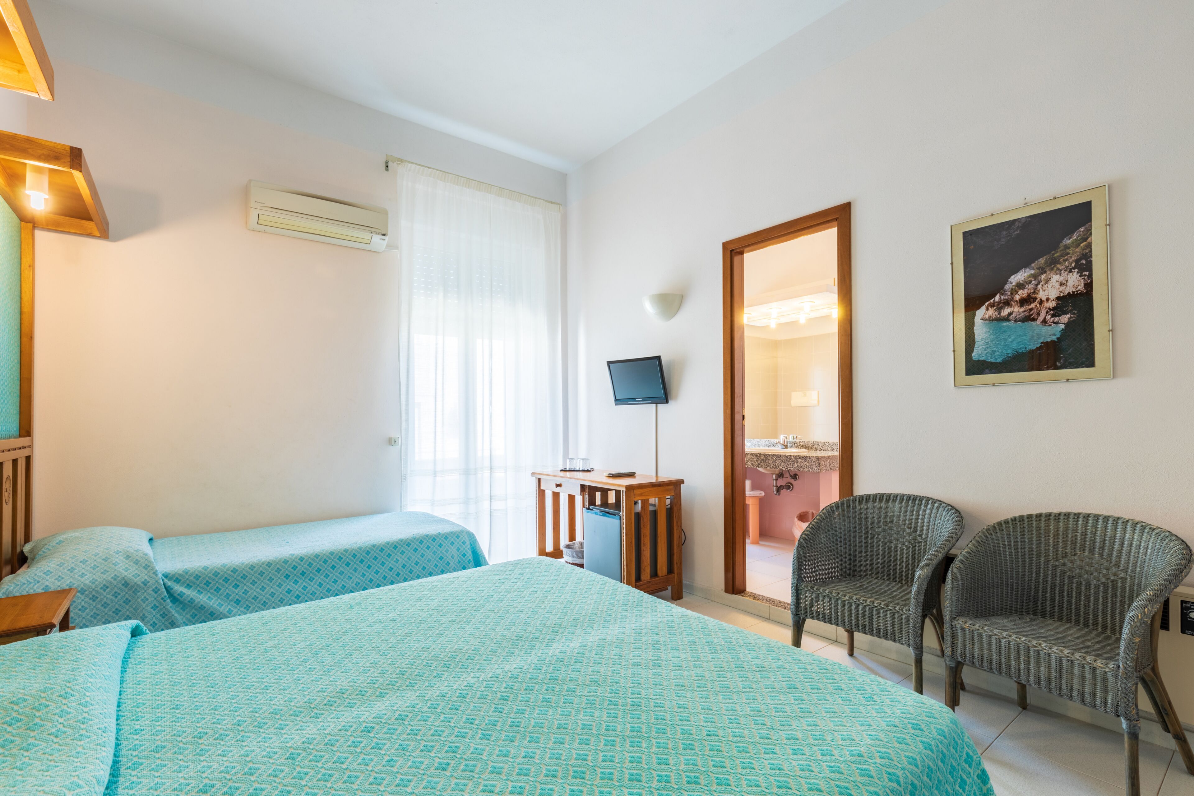 A hotel room with two single beds, a TV, a chair, and a painting on the wall.