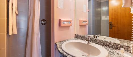 Un baño con ducha, un lavamanos con espejo y un perchero para toallas.