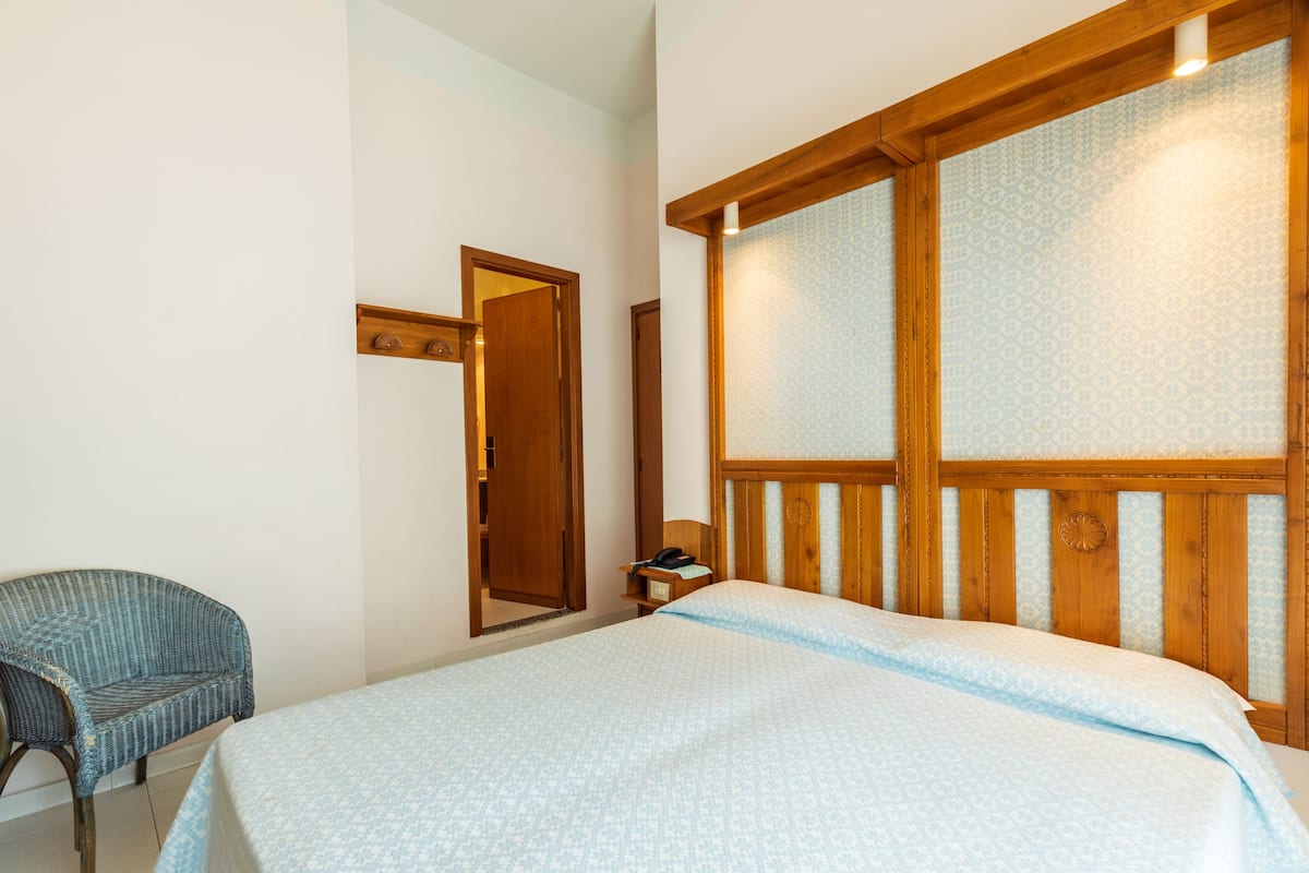 A bedroom with a bed, a chair, and a wooden headboard.