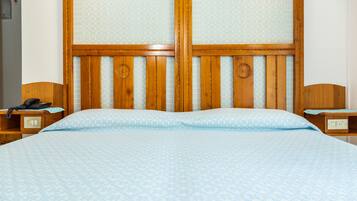 Une chambre d’hôtel avec une tête de lit en bois, un lit recouvert d’une couvre-lit à motifs, un téléphone sur la table de chevet et une petite table de nuit avec une lampe.
