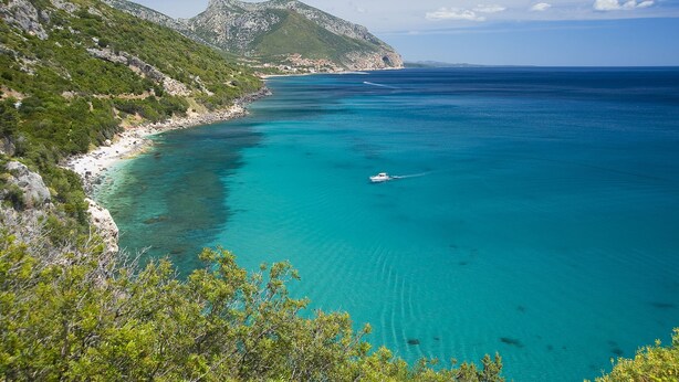 A coastal landscape with clear turquoise waters, a boat, and a mountainous backdrop. - Hotel Miramare (Dorgali)