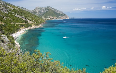 A coastal landscape with clear turquoise waters, a boat, and a mountainous backdrop.