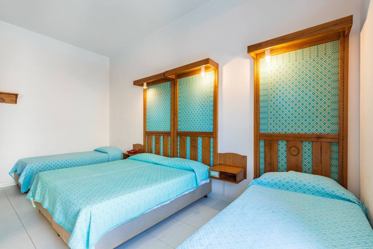 A hotel room with two single beds, wooden headboards, and a small bedside table with a lamp.
