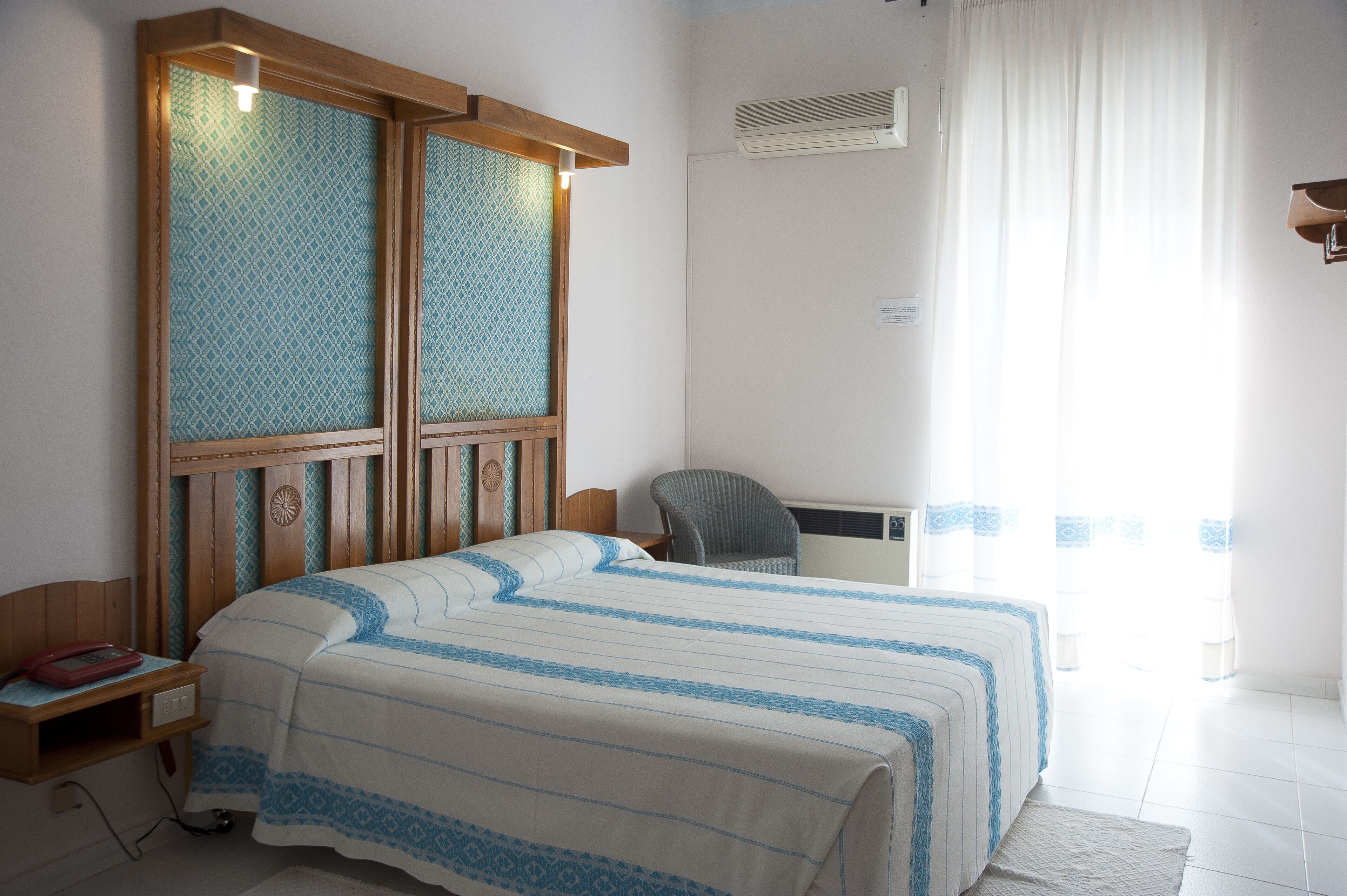 Une chambre d’hôtel avec un lit, une chaise, un bureau et une fenêtre avec des rideaux.