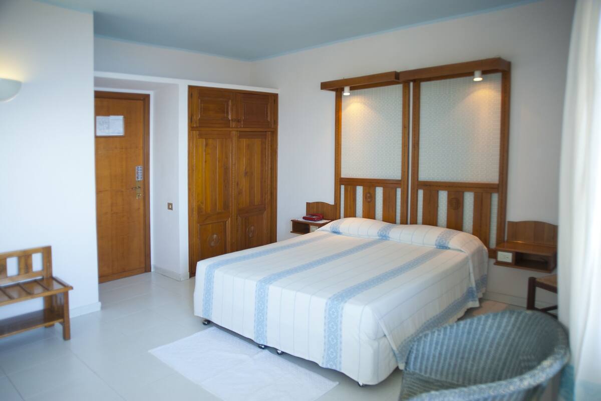 A bedroom with a large bed, wooden wardrobe, bedside tables, and a bench.
