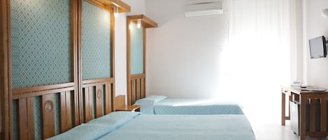 Habitación de hotel con dos camas, cabeceros de madera, un escritorio con silla y un equipo de aire acondicionado.