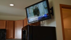 A television mounted on a wall in a room with wooden cabinets and a door. - Telluride Lodge (Watford City)