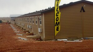A row of single-story buildings with a 'WELCOME' sign, likely a motel or hostel, with a dirt ground and no visible amenities. - Telluride Lodge (Watford City)