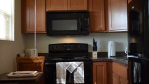 A kitchen with wooden cabinets, a black microwave, a stove, and a refrigerator. - Telluride Lodge (Watford City)