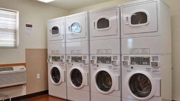 A laundry room with four stacked front-loading washing machines and a wall-mounted dryer. - Telluride Lodge (Watford City)