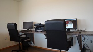 A workspace with two black office chairs, a desk with a computer monitor, a printer, and a keyboard. - Telluride Lodge (Watford City)