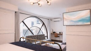 A modern bedroom with a large bed, a desk, and a view through a large window.