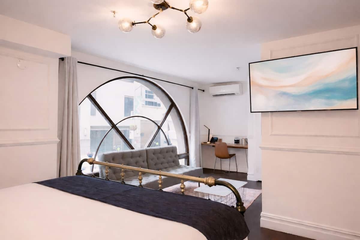 A modern bedroom with a large bed, a desk, and a view through a large window.