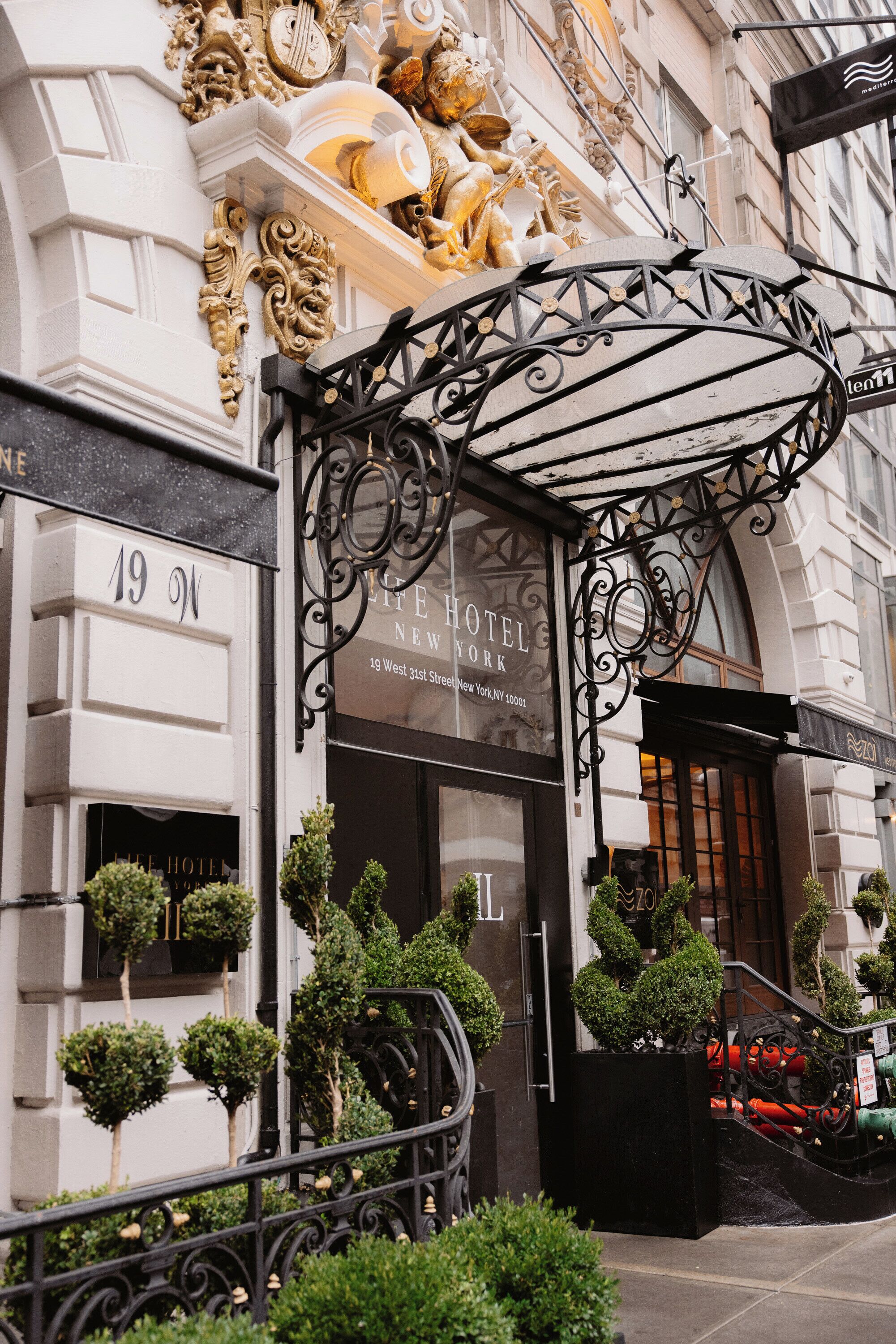 A hotel entrance with ornate metalwork, a sign reading 'Hotel New York,' and a number '19' on the building facade.