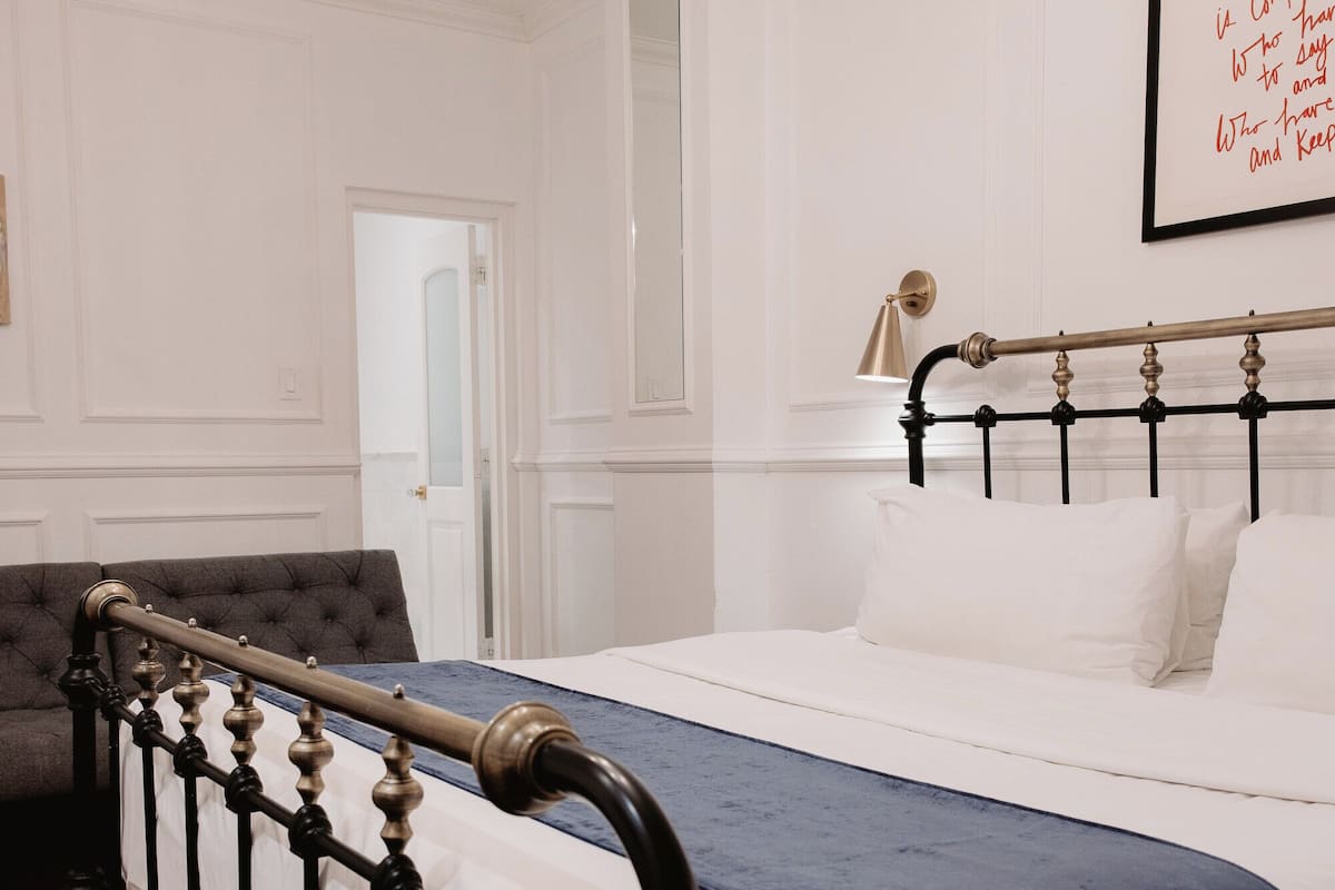 A bedroom with a bed, a bench, a chandelier, and a framed quote on the wall.