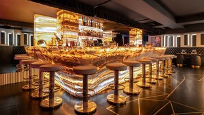 A bar area with a marble countertop, multiple stools, and a variety of bottles and glasses on shelves.