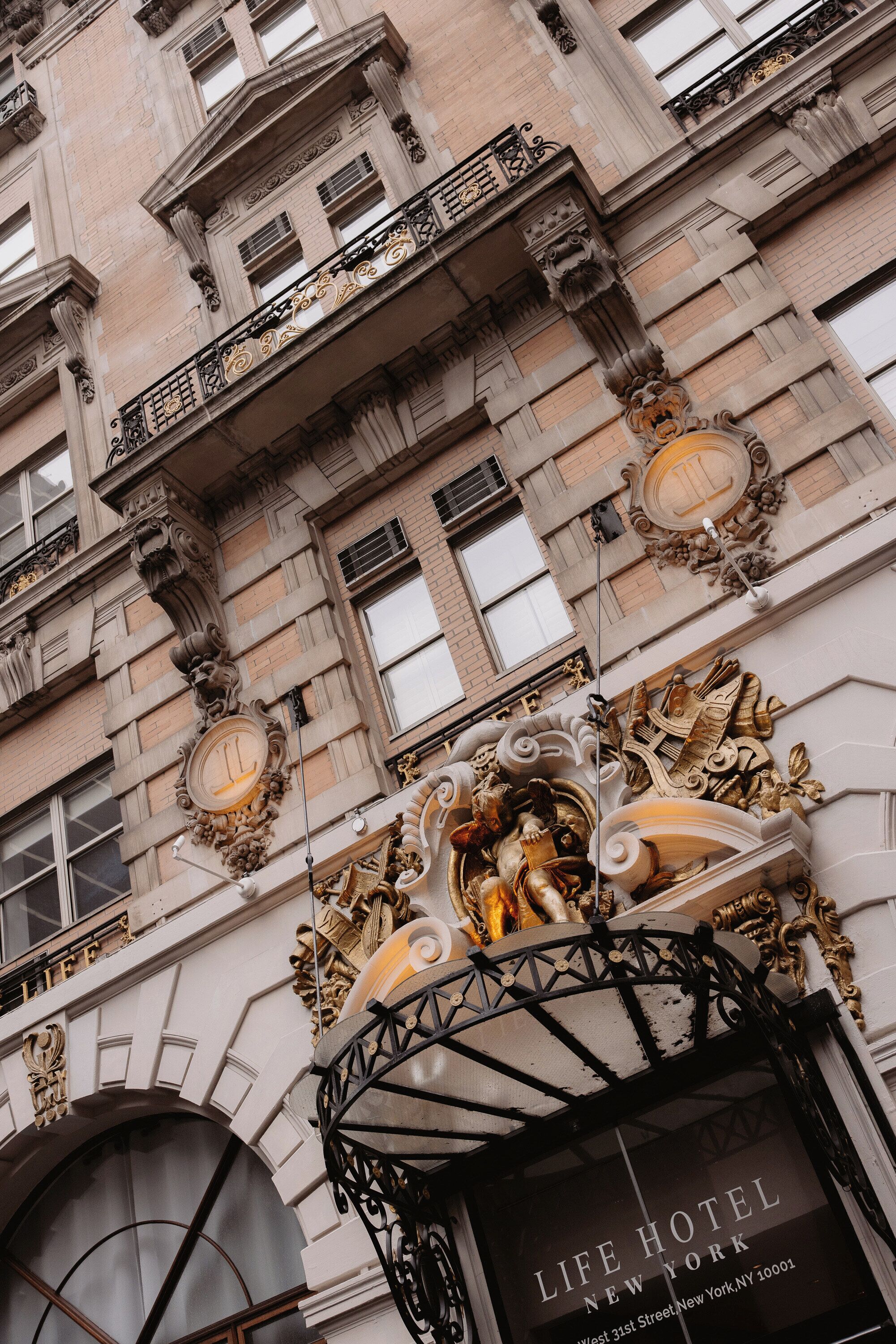 A building facade with ornate architectural details, including a prominent clock and a sign for the Life Hotel New York.
