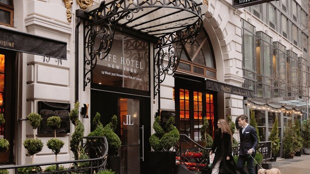 The exterior of the Life Hotel New York, featuring a classic facade, a prominent entrance with a black awning, and a well-maintained outdoor area with potted plants.