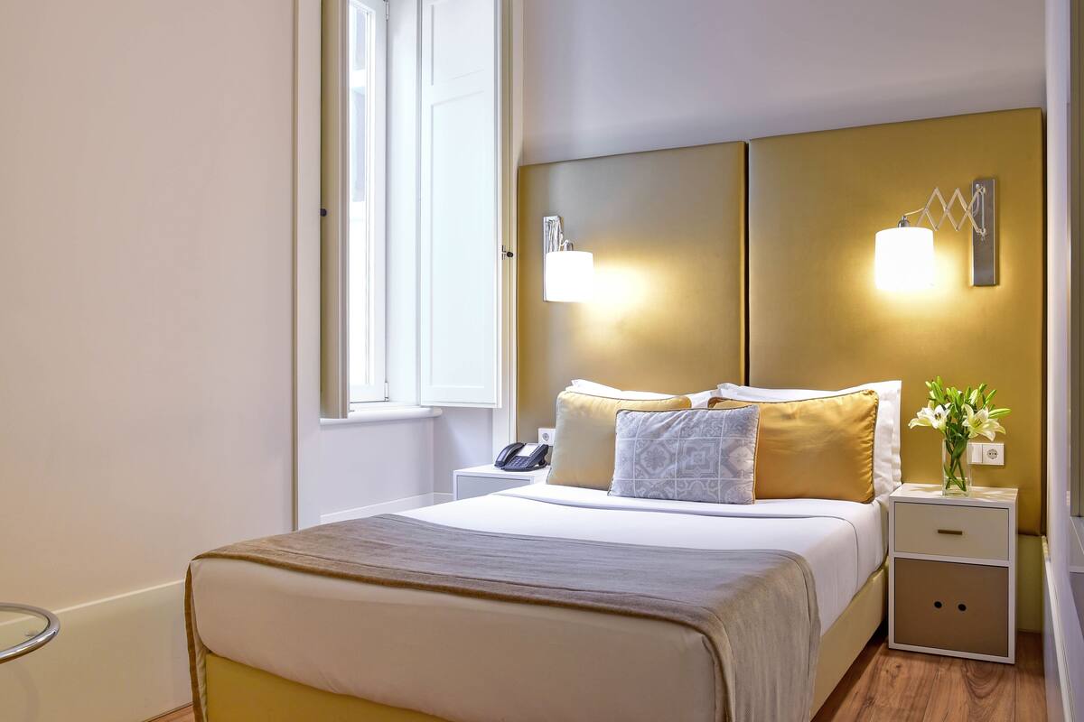 Una camera d'albergo con un letto, comodini, un tavolino con una lampada e una finestra.