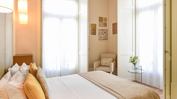 A hotel room with a bed, a chair, a small table with flowers, and artwork on the wall. - My Story Hotel Ouro (Lisbon)