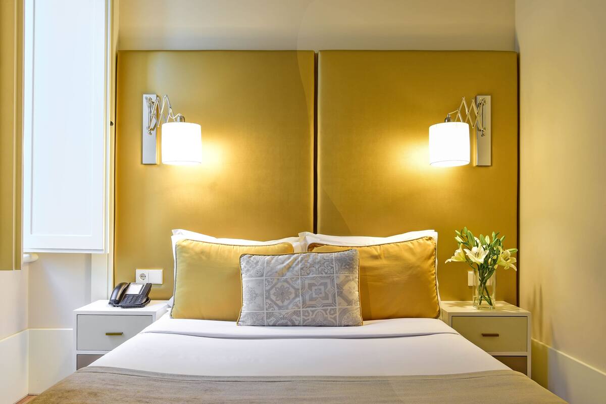 Camera d'albergo con un letto, due comodini, una lampada e un vaso con fiori.