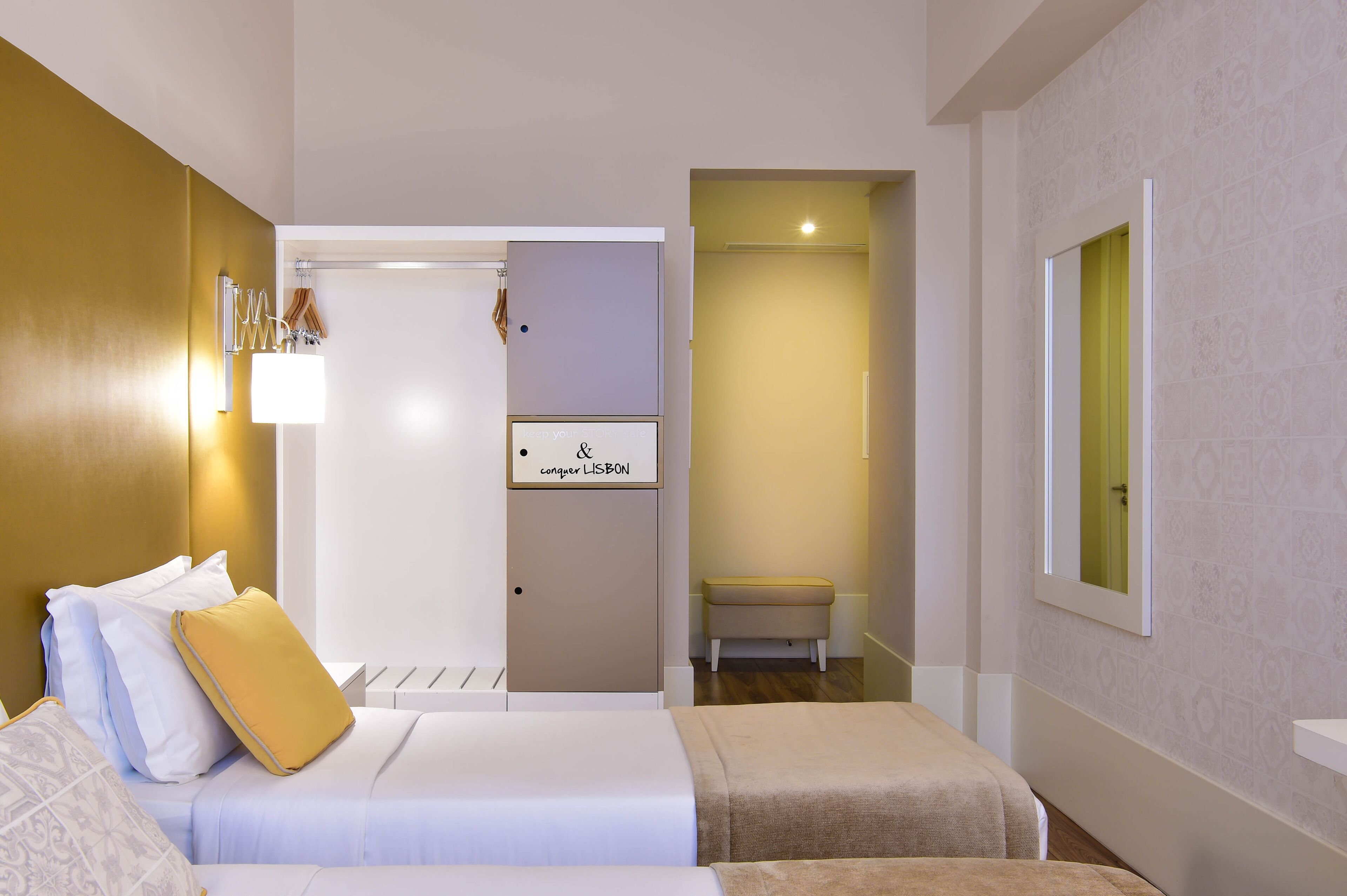 A hotel room with a bed, bedside table, and a mirror. There is a sign on the door that reads "congruent LISBON".