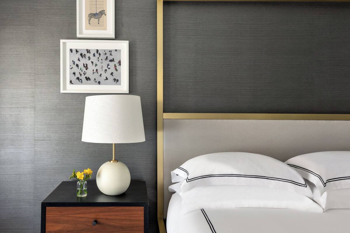 A neatly arranged bedroom with a bed, a bedside table with a lamp, and two framed artworks on the wall.