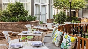 An outdoor patio area with tables and chairs, a brick wall, and greenery.
