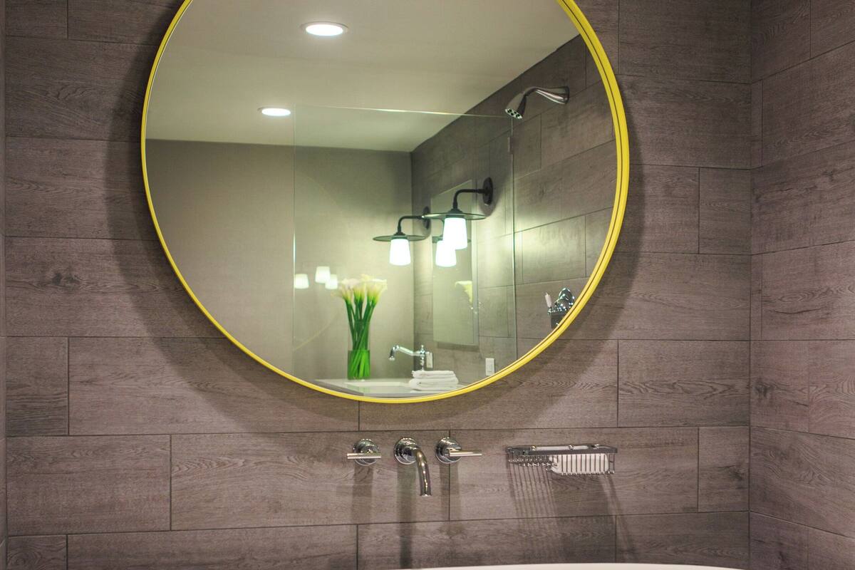 A modern bathroom with a freestanding bathtub, a round mirror with a yellow frame, and a wall-mounted towel rack.