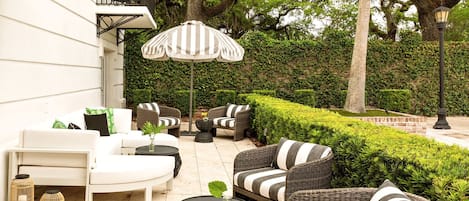 A patio area with wicker furniture, a striped umbrella, and a well-maintained hedge.
