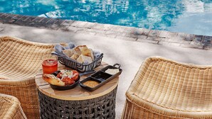 Un espacio para comer junto a la piscina con sillas de mimbre, una mesa redonda y una variedad de comida y bebidas.
