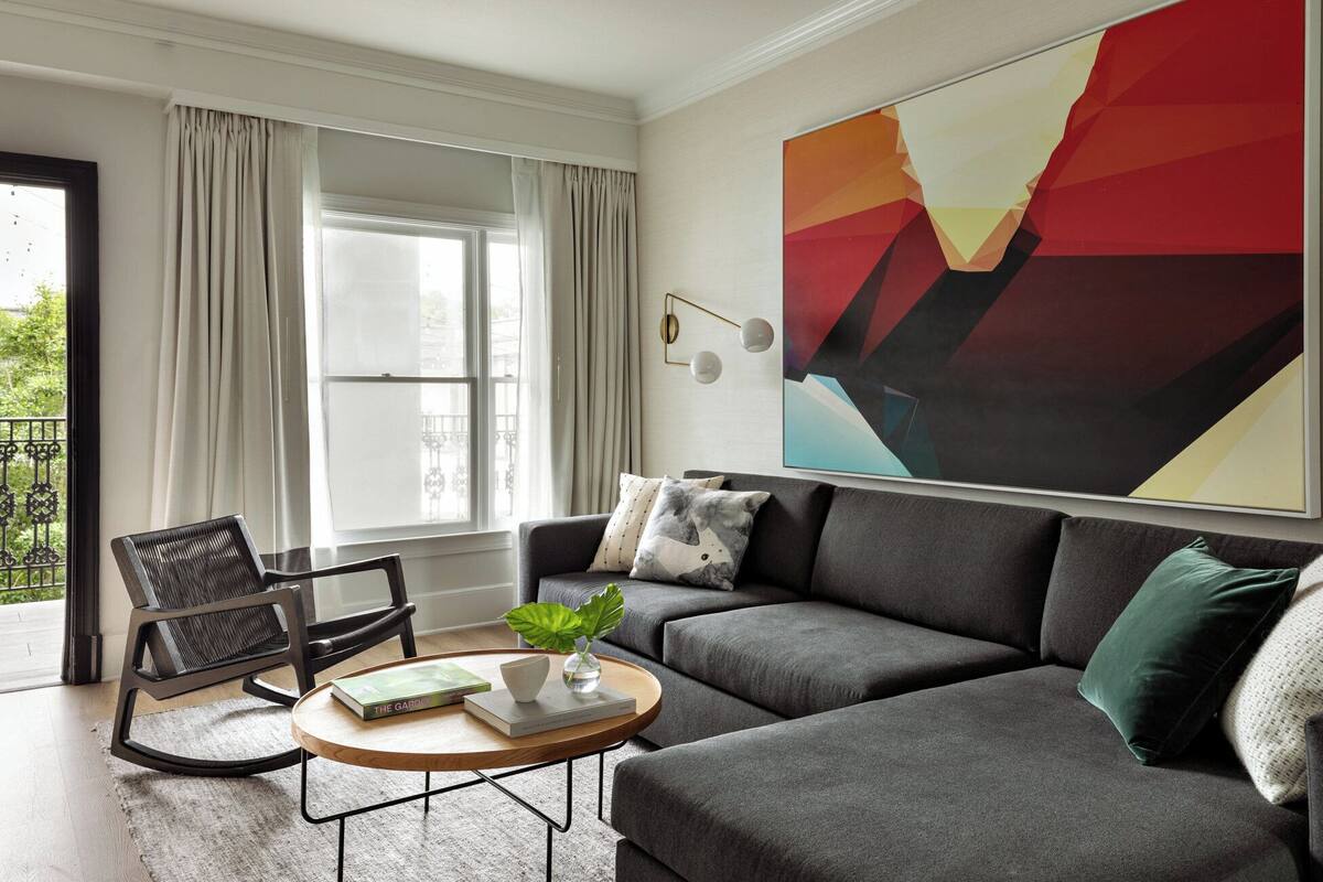 A modern living room with a grey sofa, a round wooden coffee table, and a large abstract painting on the wall.