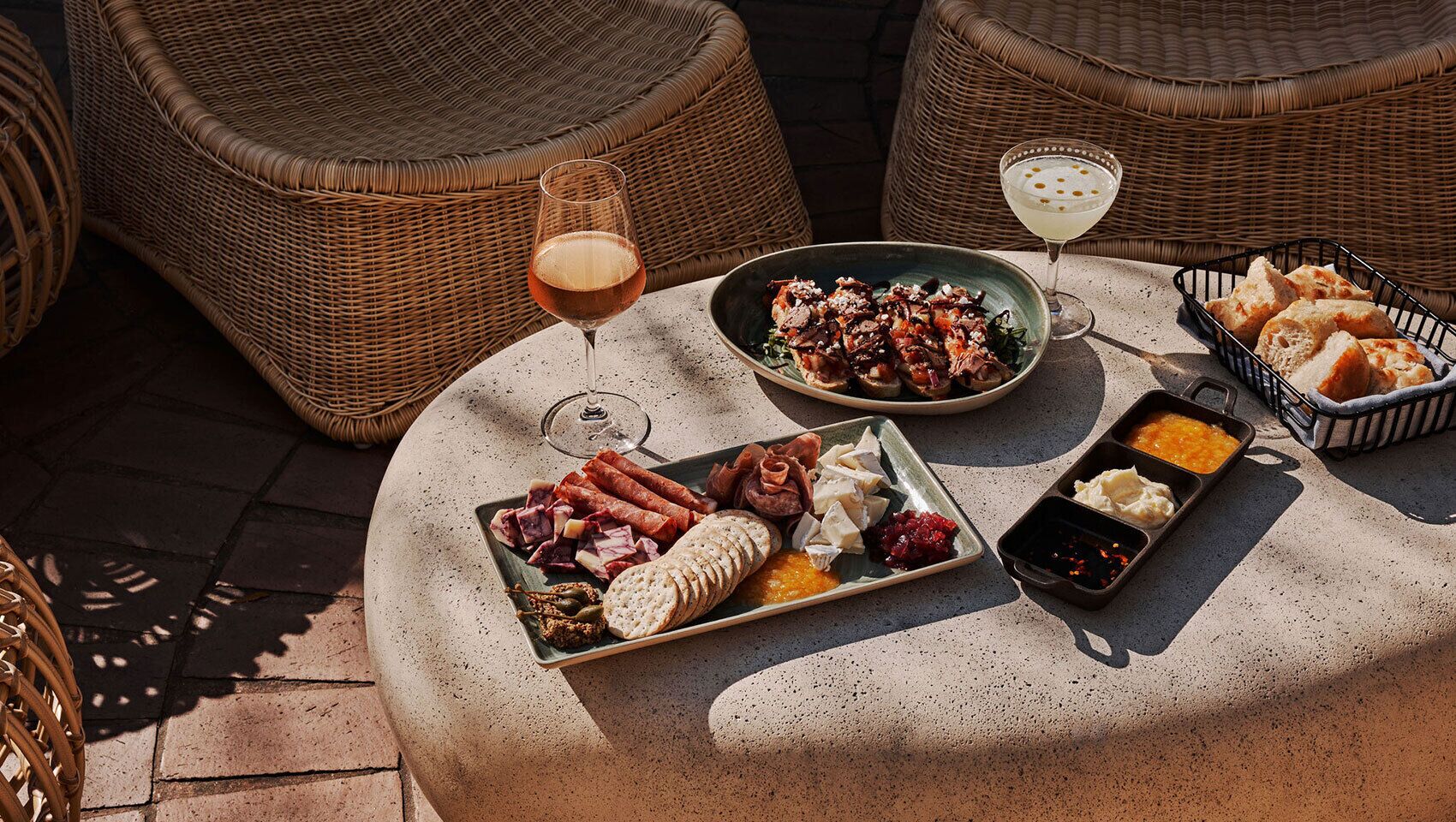Une table ronde, sur laquelle sont disposés divers aliments et boissons, entourée de chaises en osier.