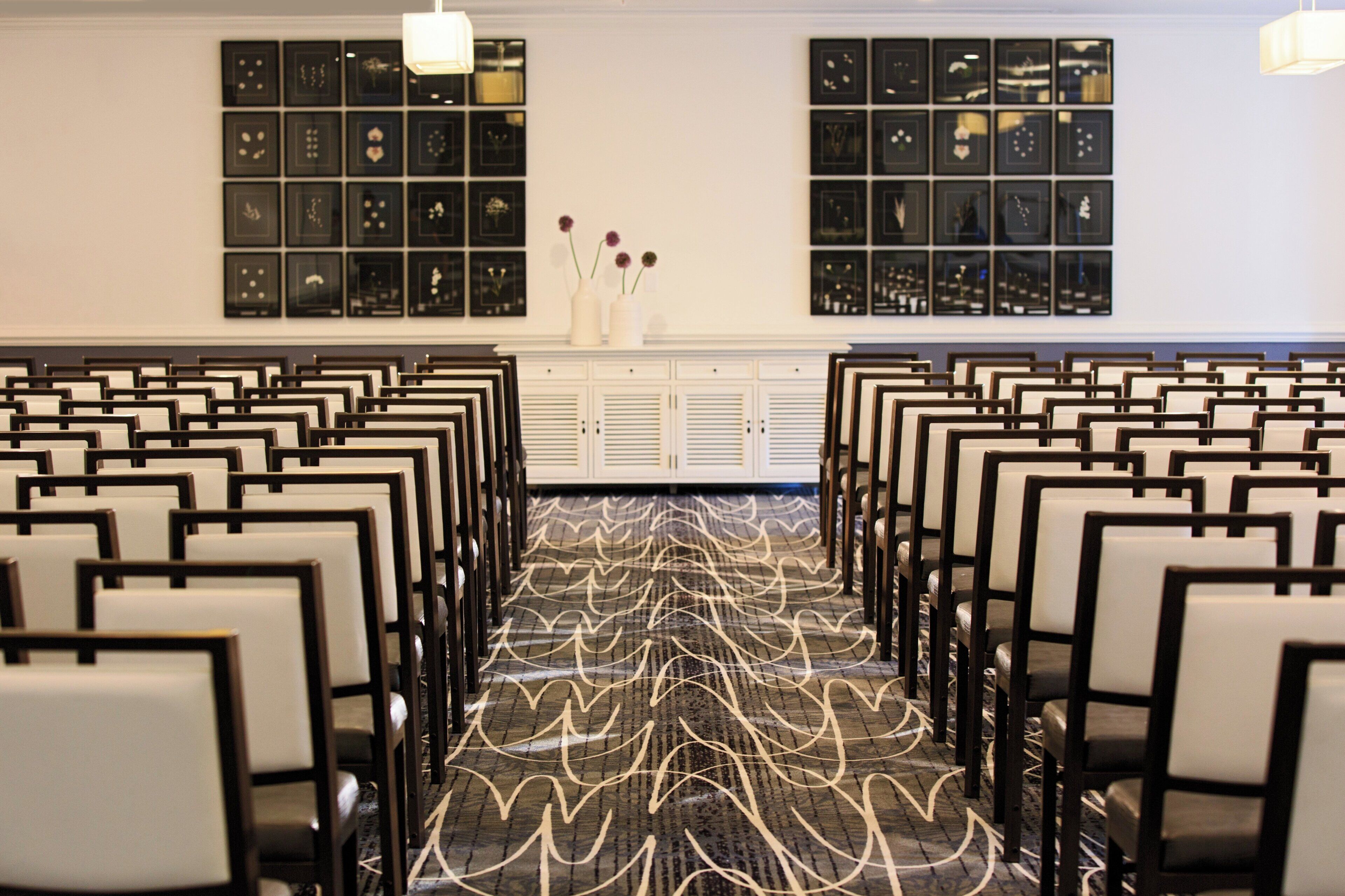 Una sala conferenze con file di sedie, una moquette decorata e quadri appesi alle pareti.