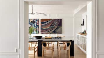 A dining area with a white table, wooden chairs, and two abstract paintings on the wall.