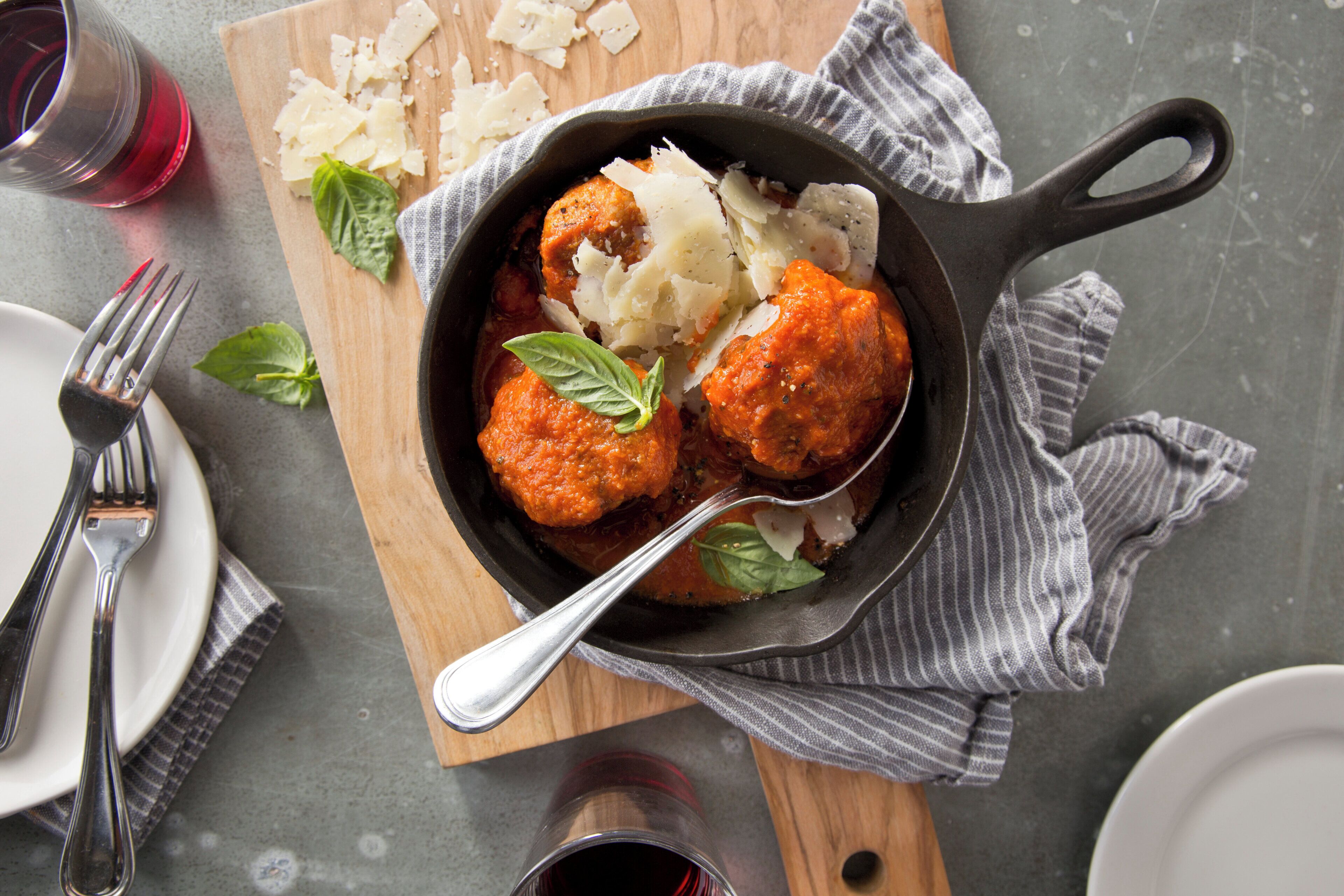 Una padella di ghisa con polpette e pasta su un tagliere di legno.
