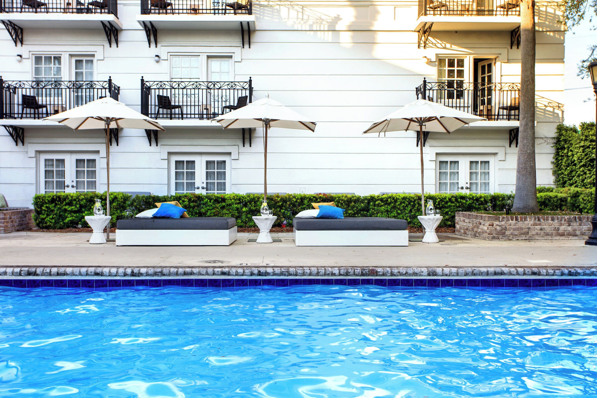 A poolside area with a white building, outdoor seating, and umbrellas.