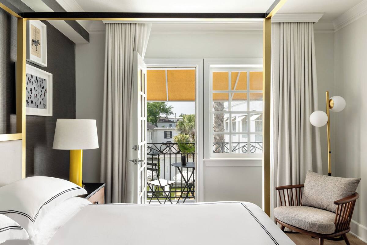 A hotel room with a bed, a chair, a lamp, a window with curtains, and a view of the outside.