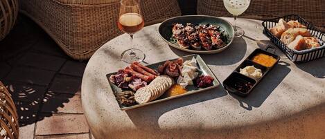 Una mesa redonda con diversos alimentos y bebidas, rodeada de sillas de mimbre.