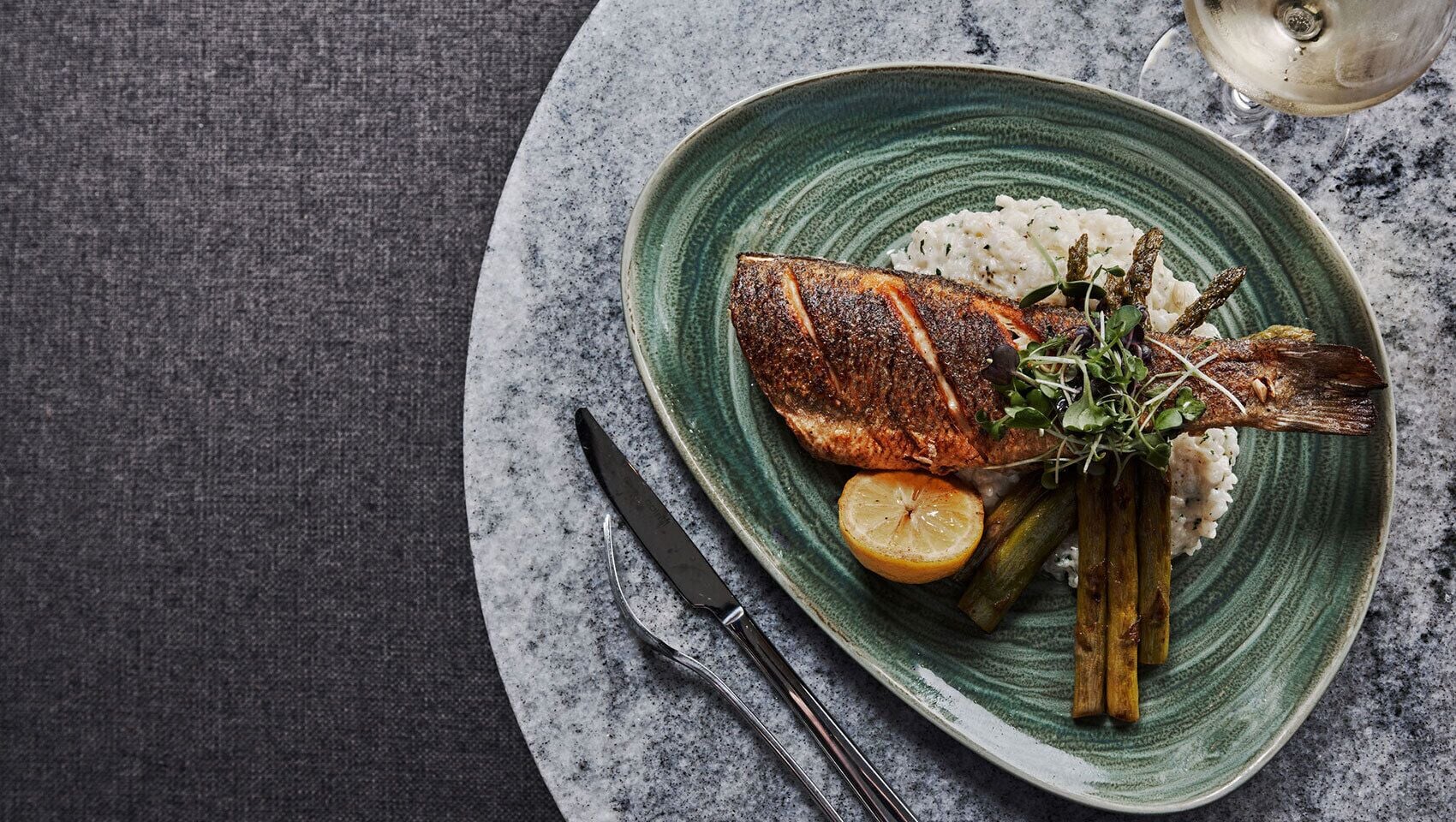 Une assiette en céramique verte contenant du poisson grillé, du riz, un quartier de citron et des asperges.