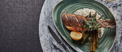 Une assiette en céramique verte contenant du poisson grillé, du riz, un quartier de citron et des asperges.