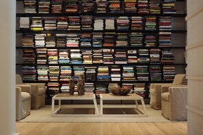 A room with a large bookshelf filled with books, two white coffee tables, and beige armchairs.