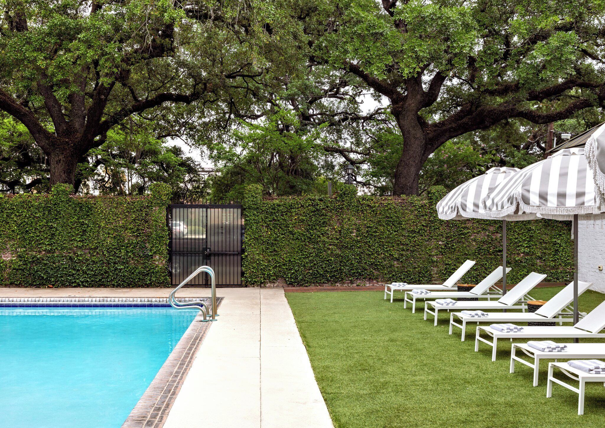 A swimming pool with a metal ladder, surrounded by a well-maintained lawn and large trees.