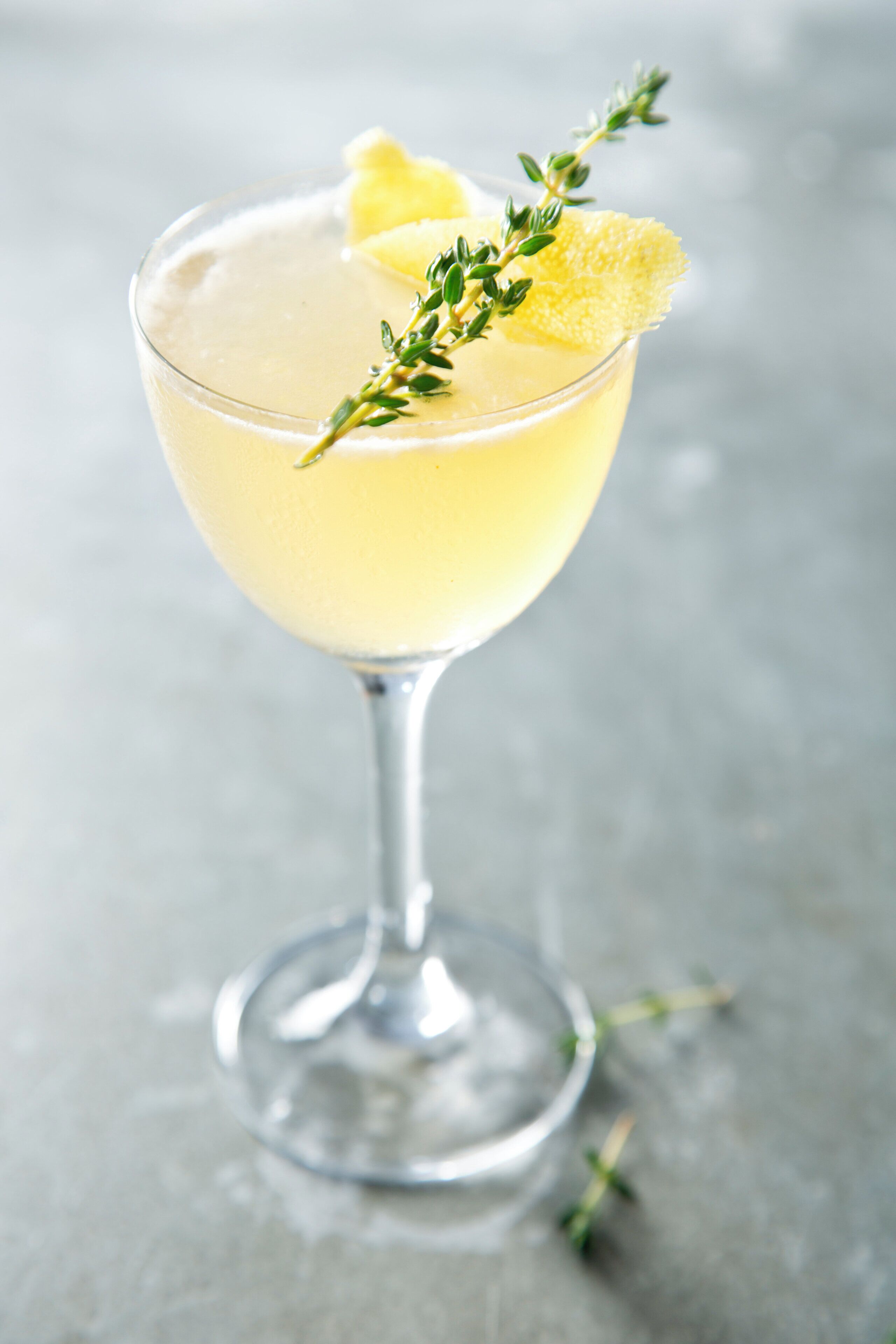 A cocktail glass with a lemon garnish and a sprig of thyme.