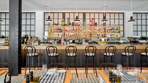 A bar area with multiple seating options, a variety of bottles and glasses on shelves, and a checkered tablecloth on the tables.