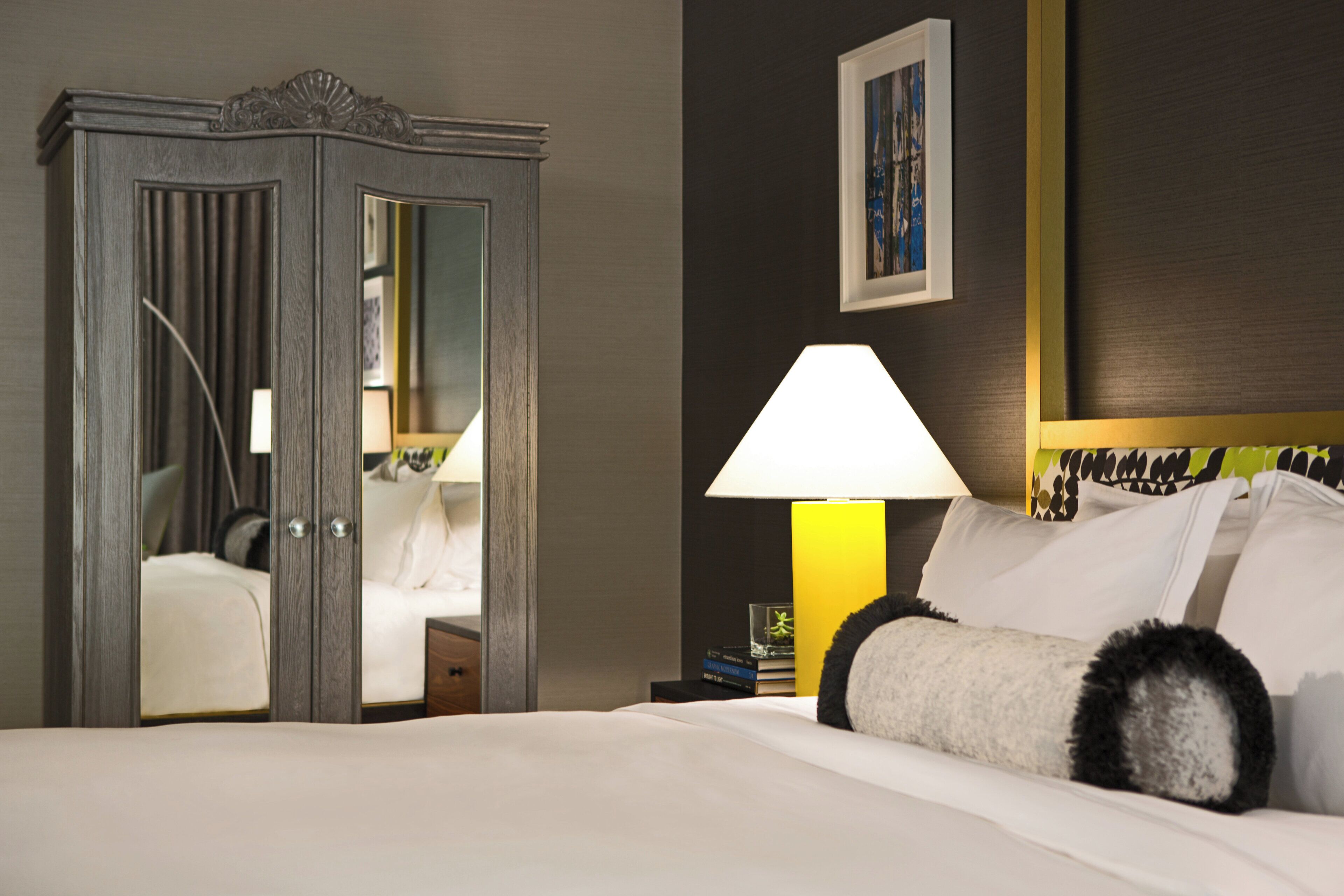 A hotel room with a bed, a nightstand, a lamp, a wardrobe, and a framed picture on the wall.