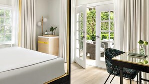 Habitación de hotel con cama, escritorio con silla, mesita con un florero y vista al exterior por una puerta.