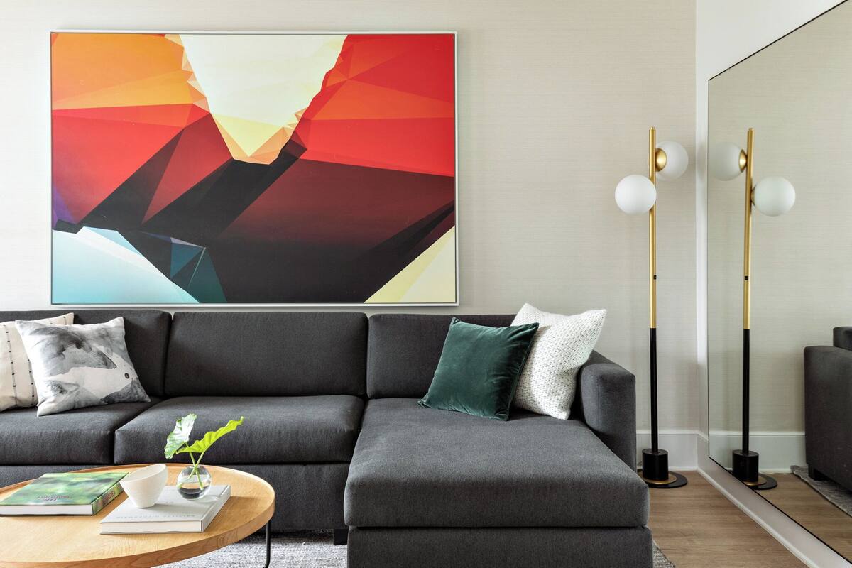 A modern living room with a grey sectional sofa, a round wooden coffee table, and a large abstract painting on the wall.